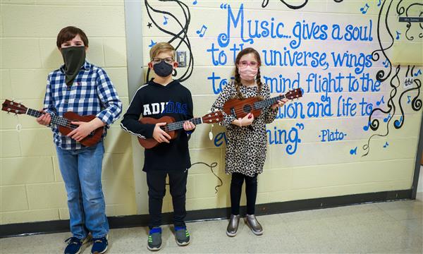 students hold ukuleles and stand against wall